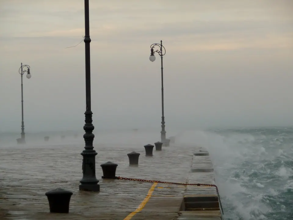 Il Molo Audace di Trieste con la Bora: lampioni e bitte nella foschia, e il mare bianco di schiuma che spruzza sulla banchina