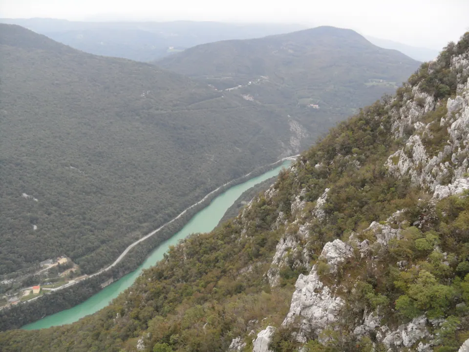 Dall'alto di un pendio roccioso, la valle con il fiume verde-azzurro che scorre fra monti boscosi.
